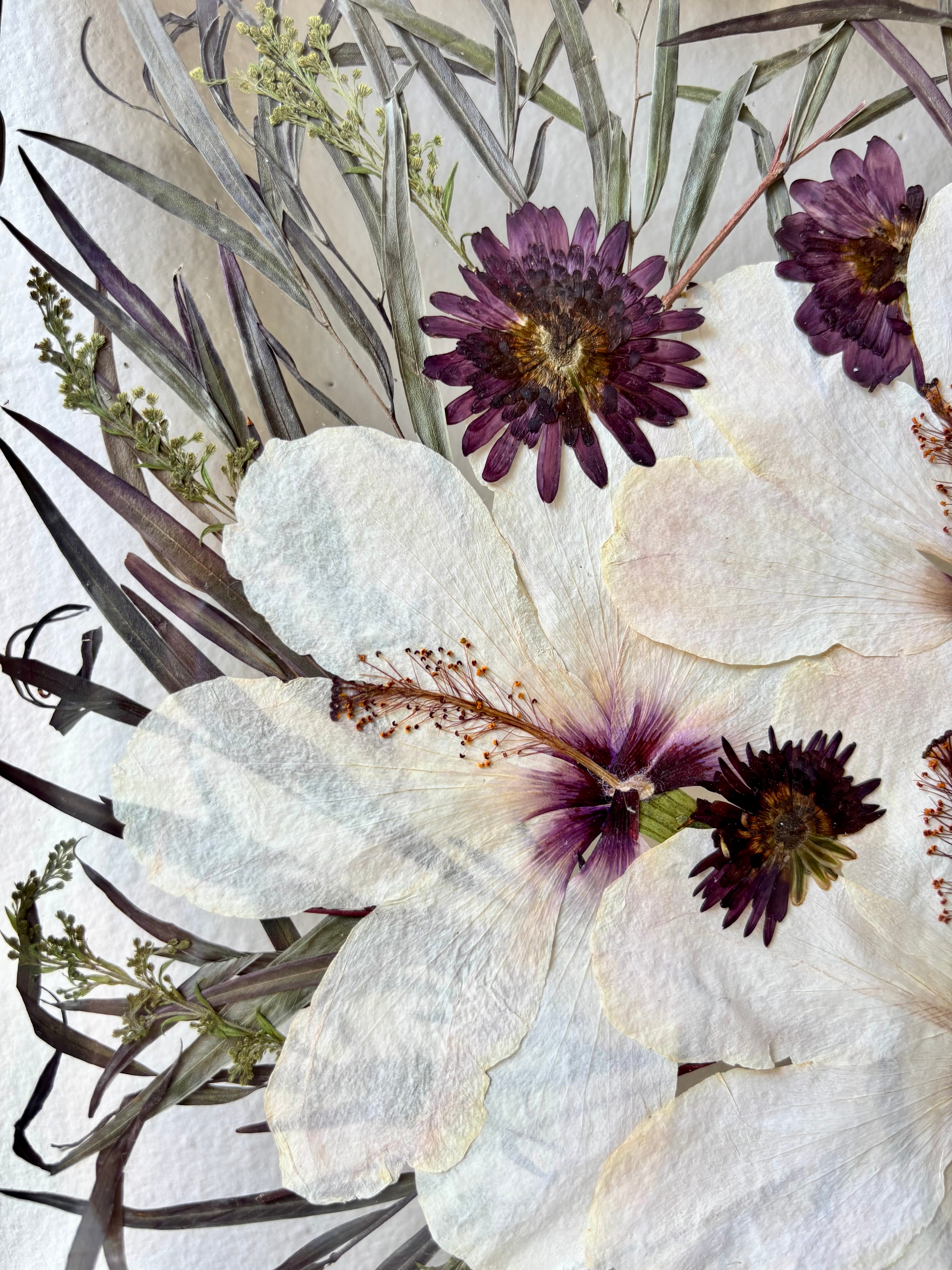 Close-up of pressed wedding flowers with white, purple, and green hues on a textured background.