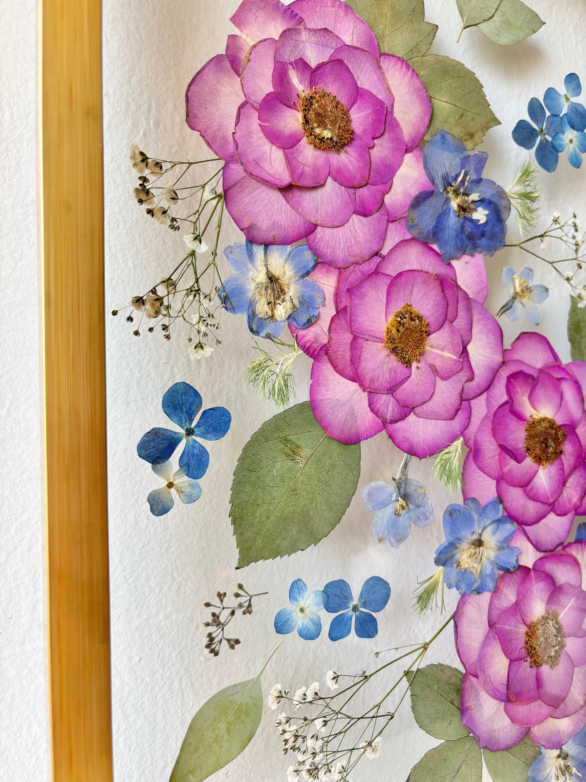 A close up of a pressed wedding bouquet preserved in a floating frame lined with wooden gold.