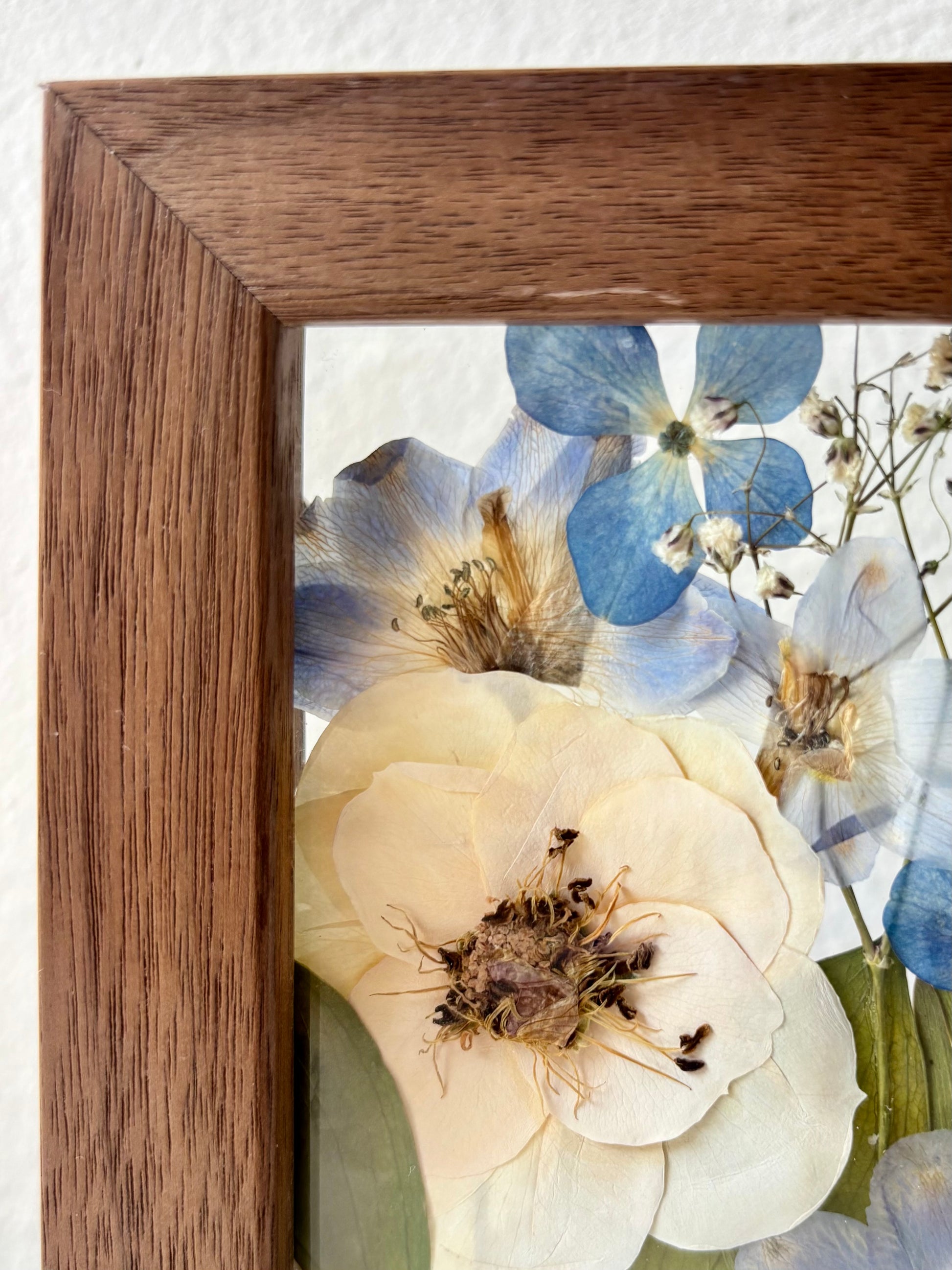 Close-up of a walnut wooden frame with a pressed flowers from a wedding bouquet featuring small blue and white flowers.