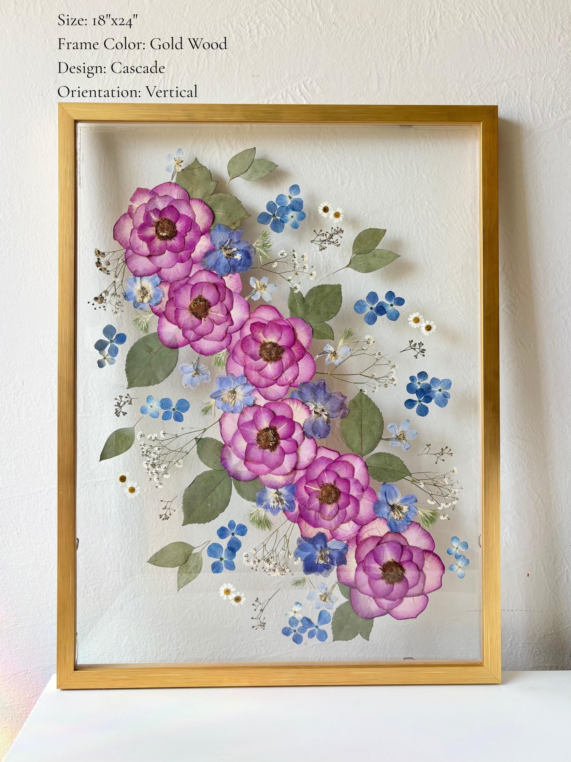 Bridal bouquet preservation pressed into glass frame wall art in wood gold framing. Purple and blue preserved bouquet in a cascade style.