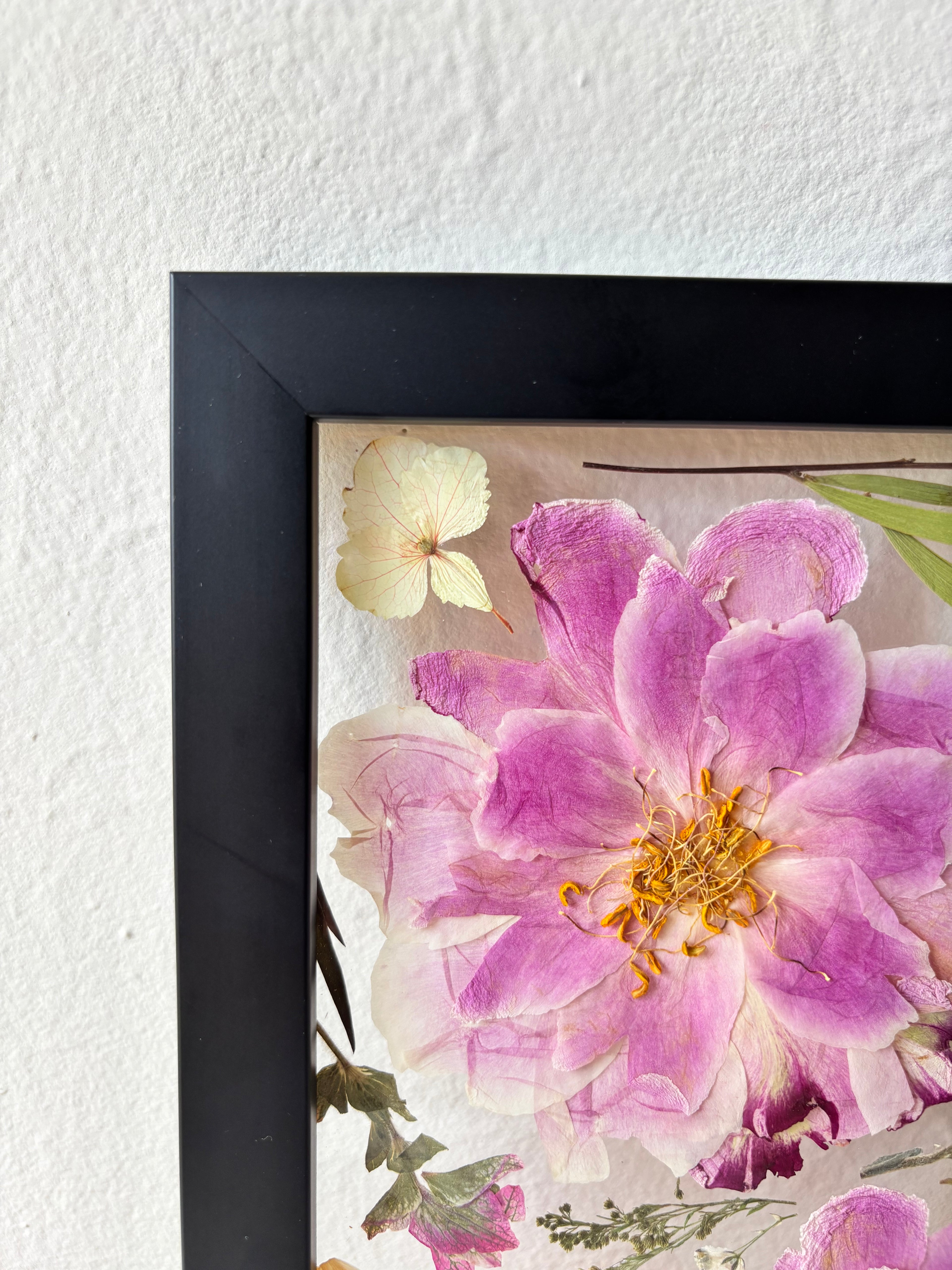 A close up of a black floating frame containing pressed wedding flowers.