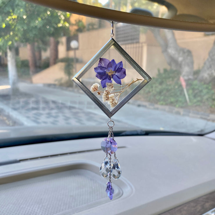Purple car decor. A handmade sun catcher with a floral design, featuring a purple flower and clear crystals, hanging from a car's rear view mirror.