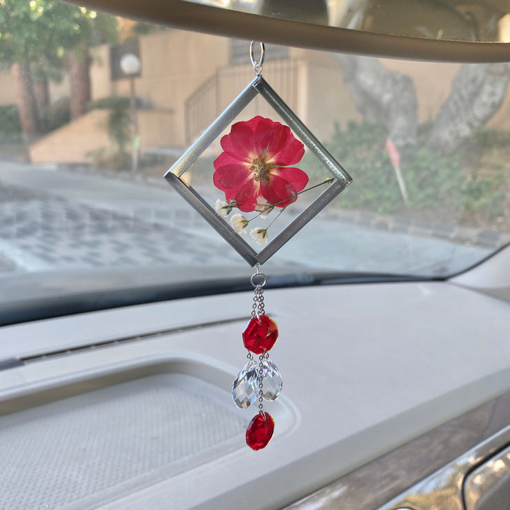 Red car decor. A handmade sun catcher with a floral design, featuring a red flower and clear crystals, hanging from a car's rearview mirror.