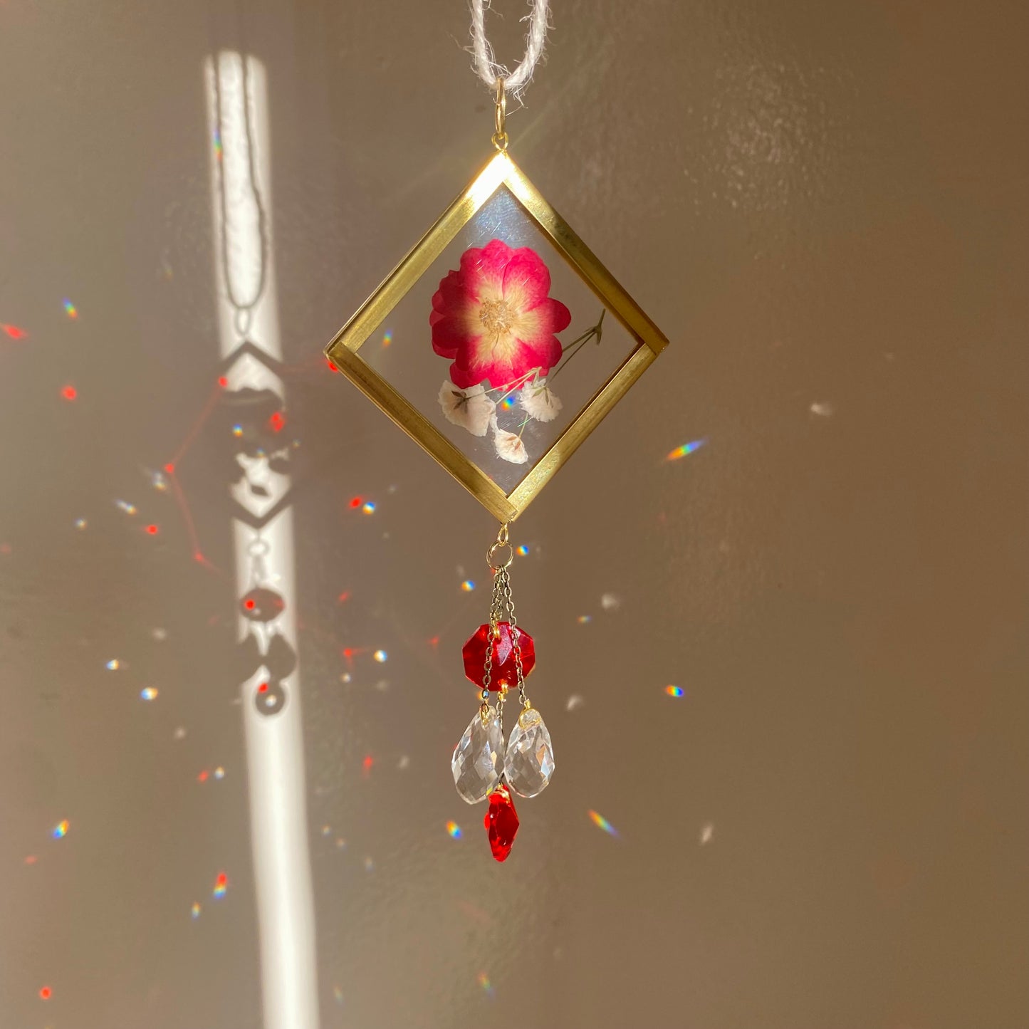 Girly red car decor. A handmade sun catcher with a floral design, featuring a red flower and clear crystals, hanging from a car's rear view mirror.